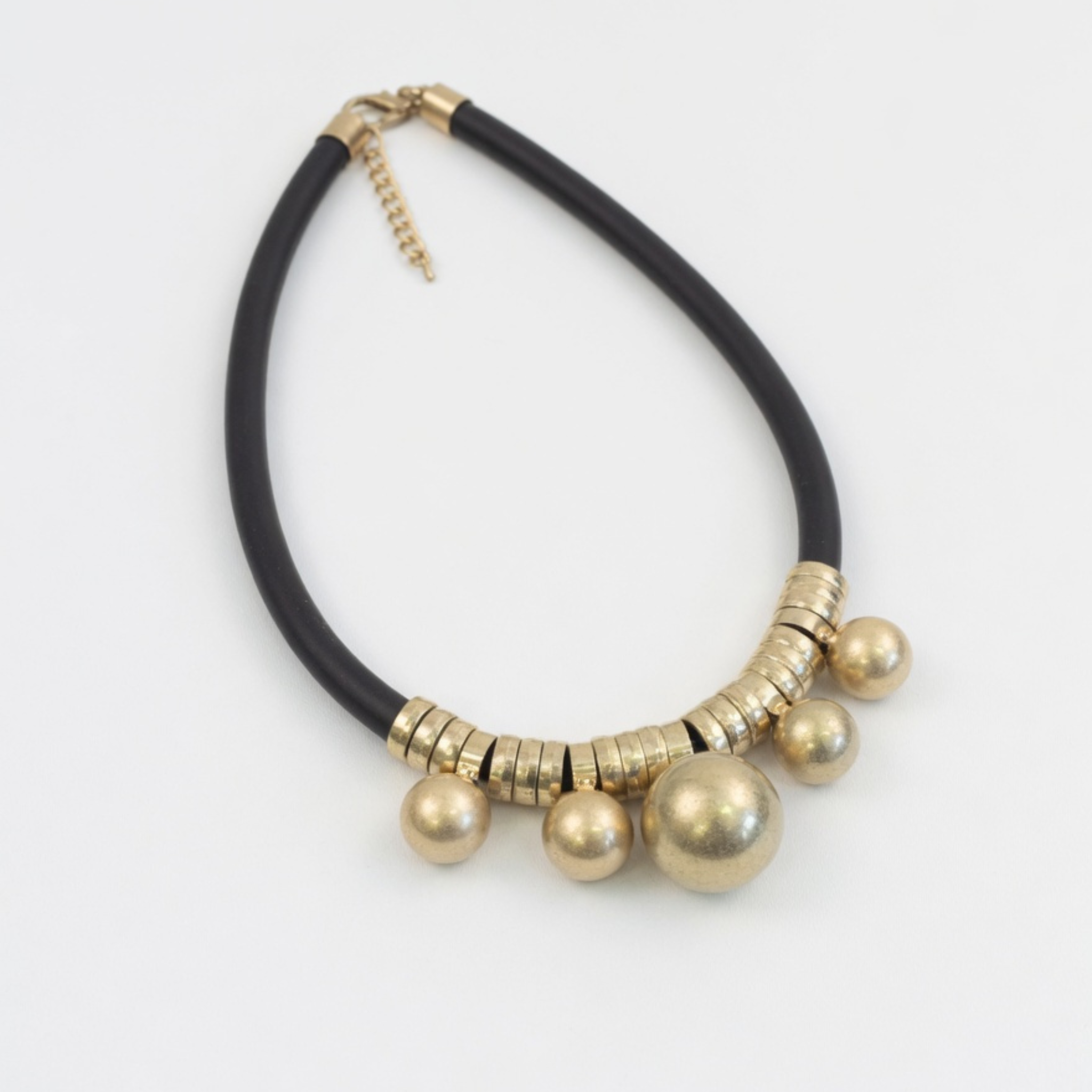 Schwarze Kette mit goldfarbenen Kugeln und Verschluss auf hellem Hintergrund
