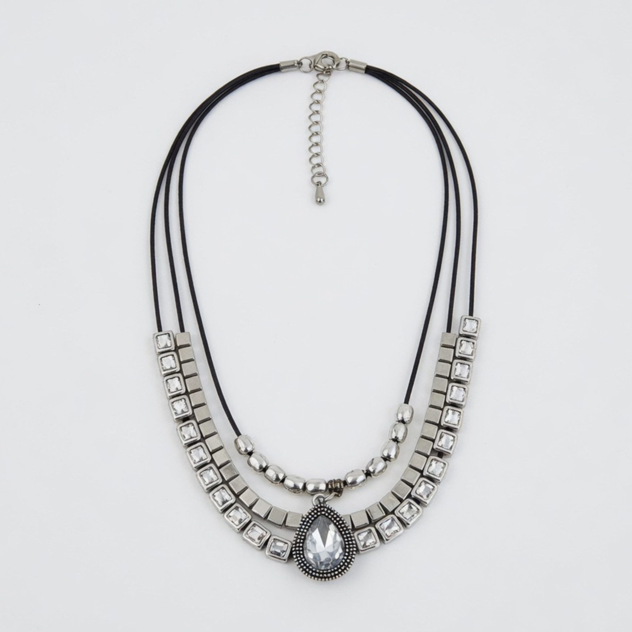Produktfoto einer dreireihigen Statement-Kette mit schwarzen Kordeln, quadratischen Gliedern und einem tropfenförmigen Kristall-Anhänger auf weißem Grund.