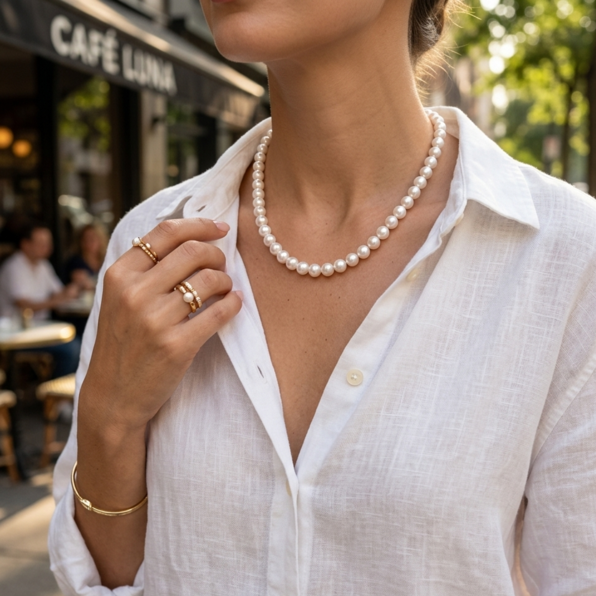 Weiße Perlenkette am Hals, getragen zu heller Bluse in sonniger Café-Atmosphäre