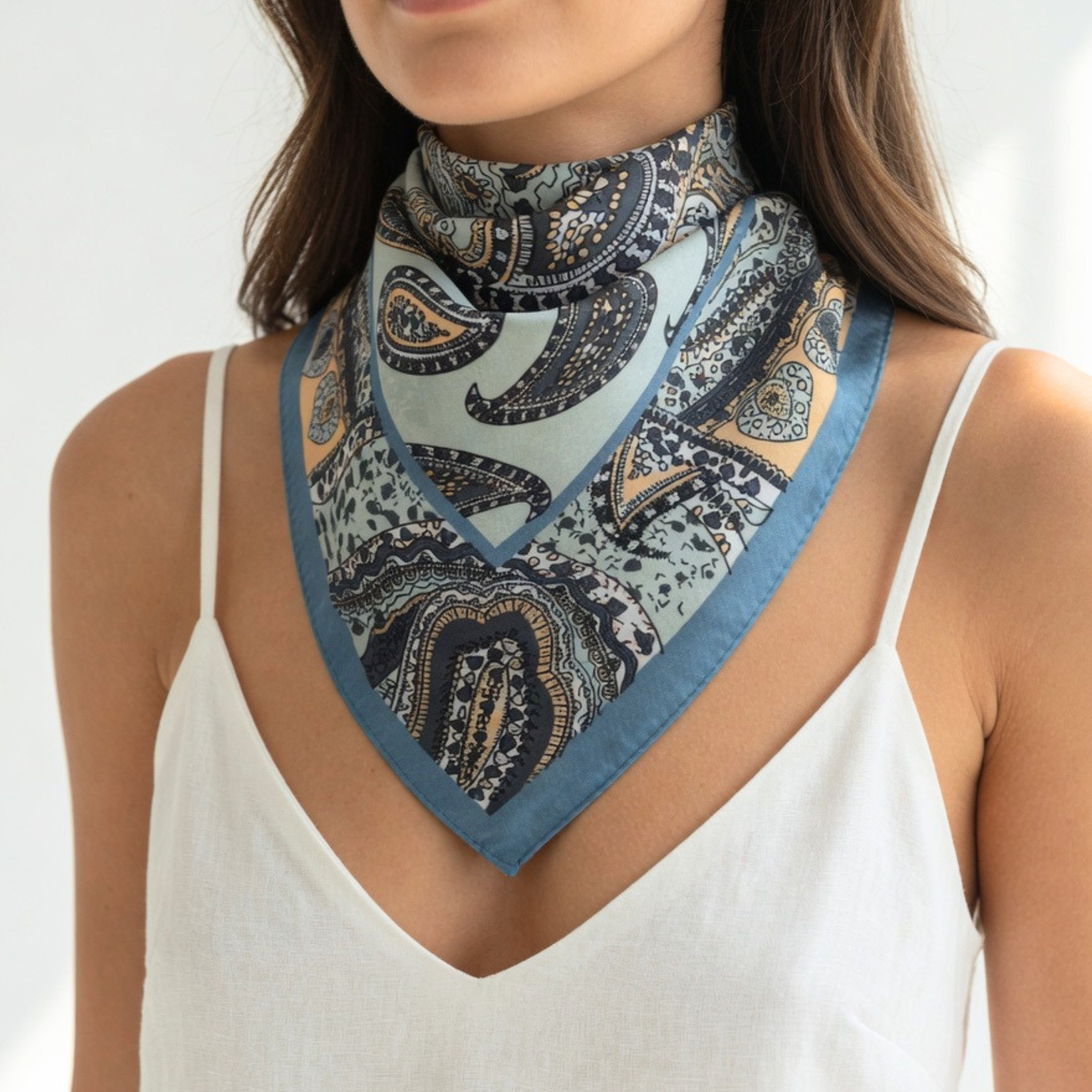 Ein Model trägt das mintfarbene Paisley-Tuch als Dreieck über einem weißen Top. Die harmonischen Blau- und Erdtöne des Musters kommen auf dem hellen Untergrund besonders gut zur Geltung und machen es zu einer stilvollen Geschenkidee.