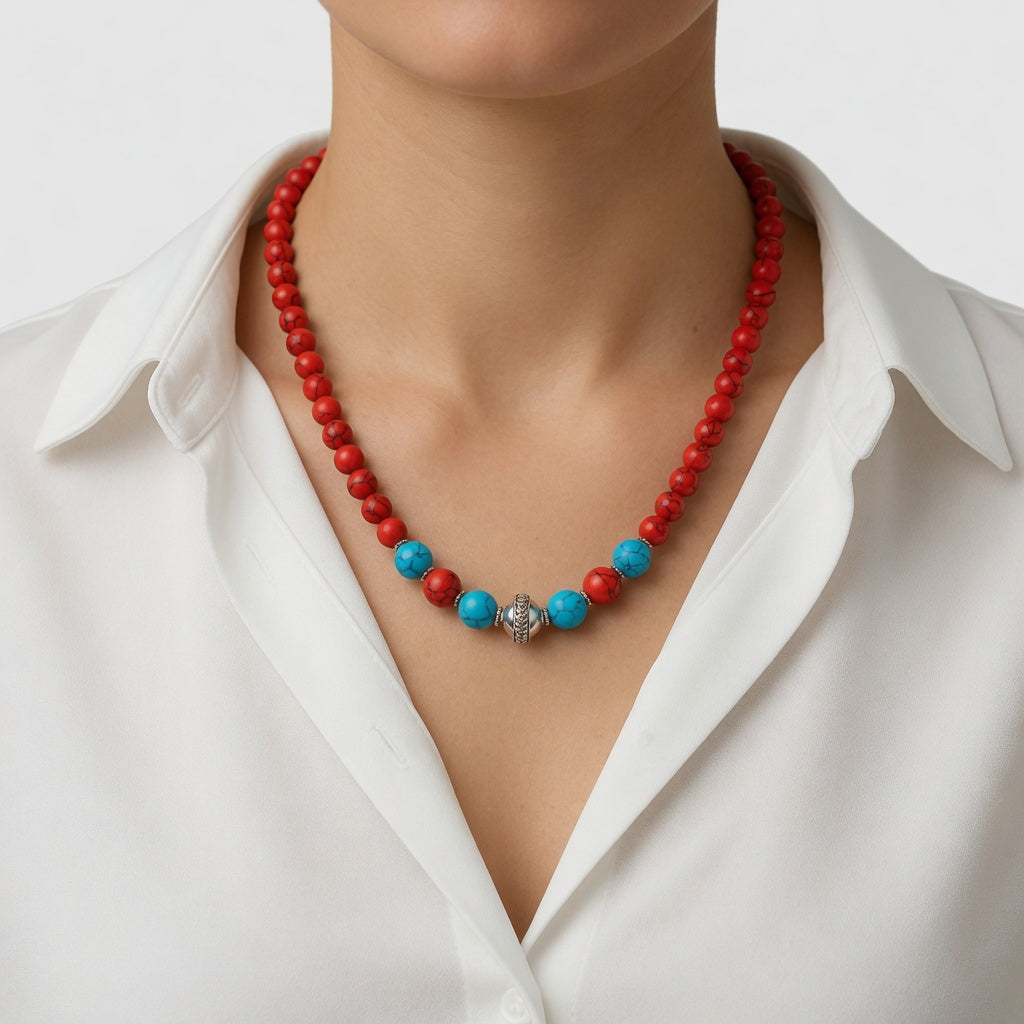 Nahaufnahme einer Frau in einem weißen Hemd, die eine rote Perlenkette mit blauen Türkis-Akzenten und einem zentralen Silberelement trägt.