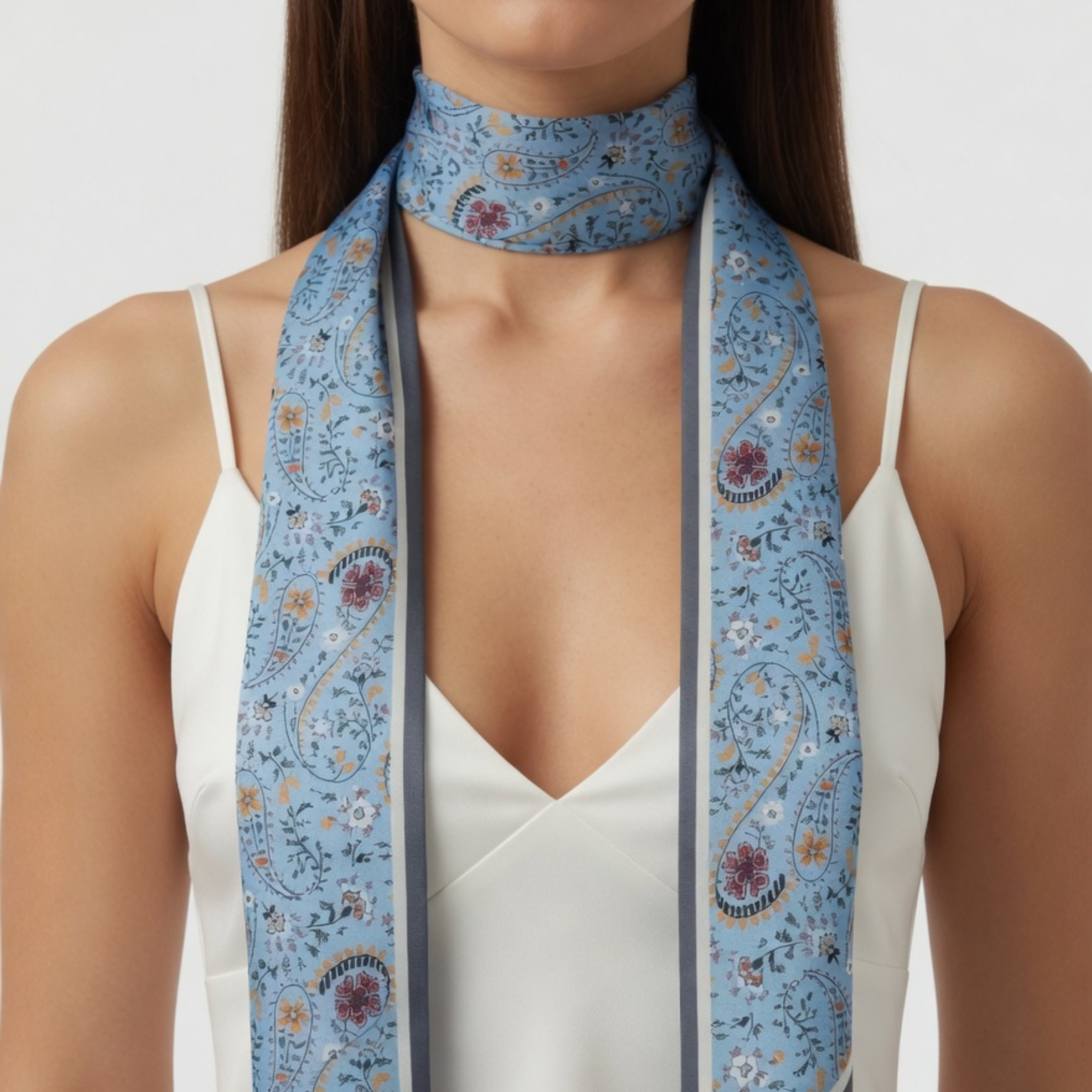 Ein schmales Paisley-Bandana, das einmal locker um den Hals gewickelt ist, wobei die langen Enden symmetrisch über ein weißes Trägertop herabhängen. Das Design besticht durch filigrane florale Ranken auf einem lichtblauen Untergrund mit dunkelgrauer Kontrastkante.
