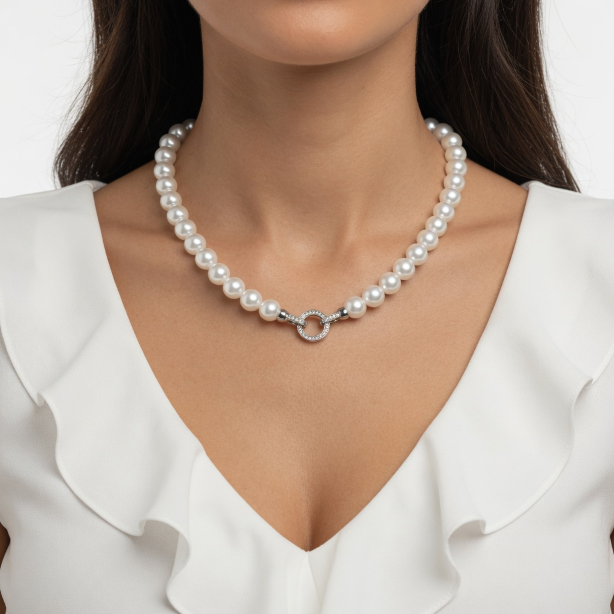 Nahaufnahme einer Frau, die die weiße Perlenkette zu einer eleganten weißen Bluse mit Rüschenausschnitt trägt. Der dekorative silberne Ringverschluss ist mittig platziert und dient als zentrales Schmuckelement.