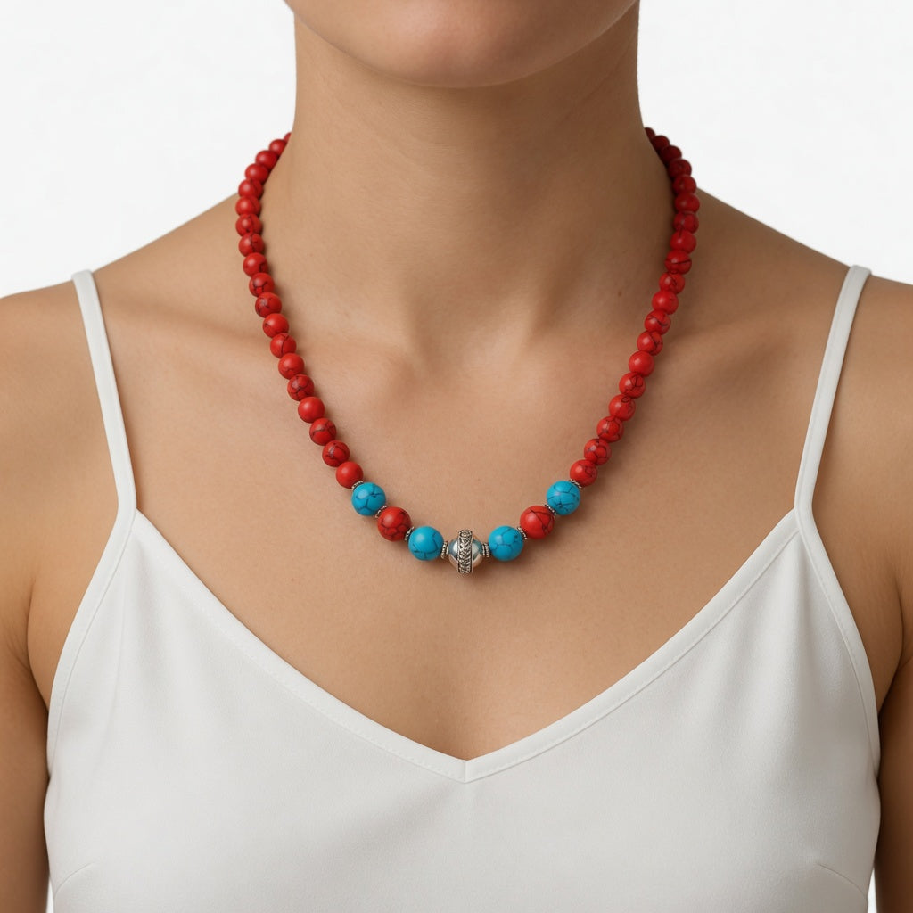 Frontalansicht einer Frau in einem weißen Spaghettiträger-Top, die eine rote Howlith-Kette mit blauen Perlen und silbernem Zwischenelement präsentiert.