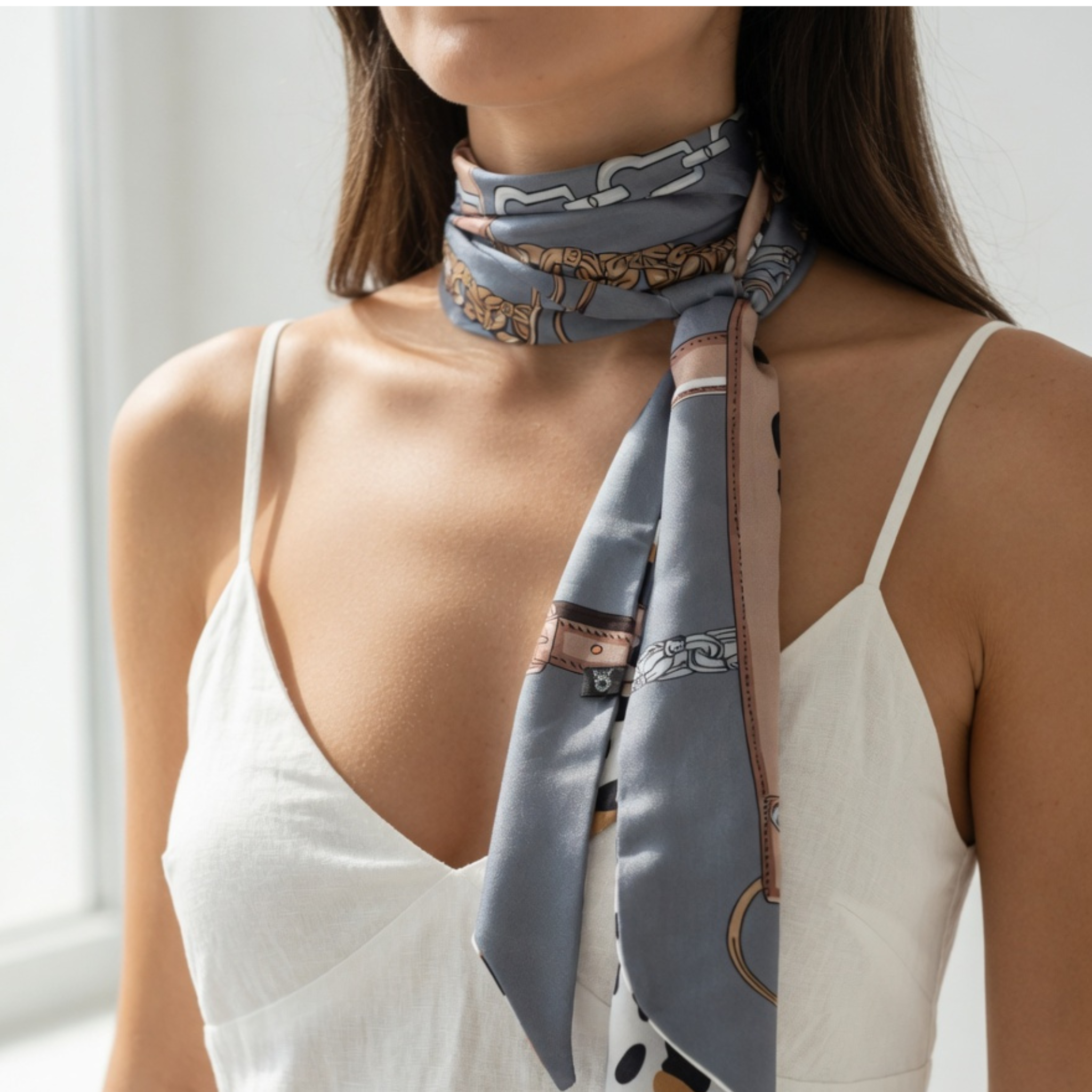 Nahaufnahme einer Frau, die das schmale Bandana eng um den Hals gewickelt trägt. Die blau-graue Seite mit den filigranen Kettenelementen liegt außen, während die Enden locker über ein weißes Sommertop fallen.