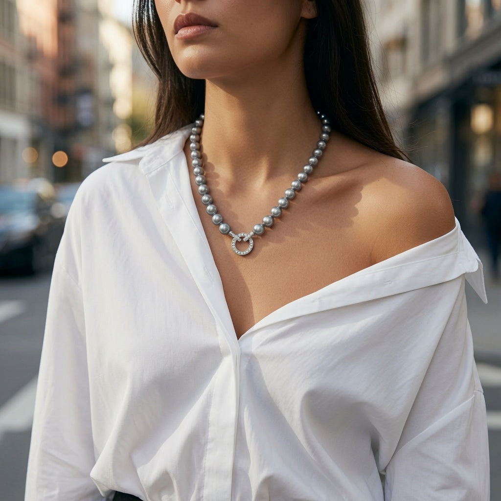 Graue Perlenkette mit silberfarbenem Ringdetail, getragen zu weißer Bluse