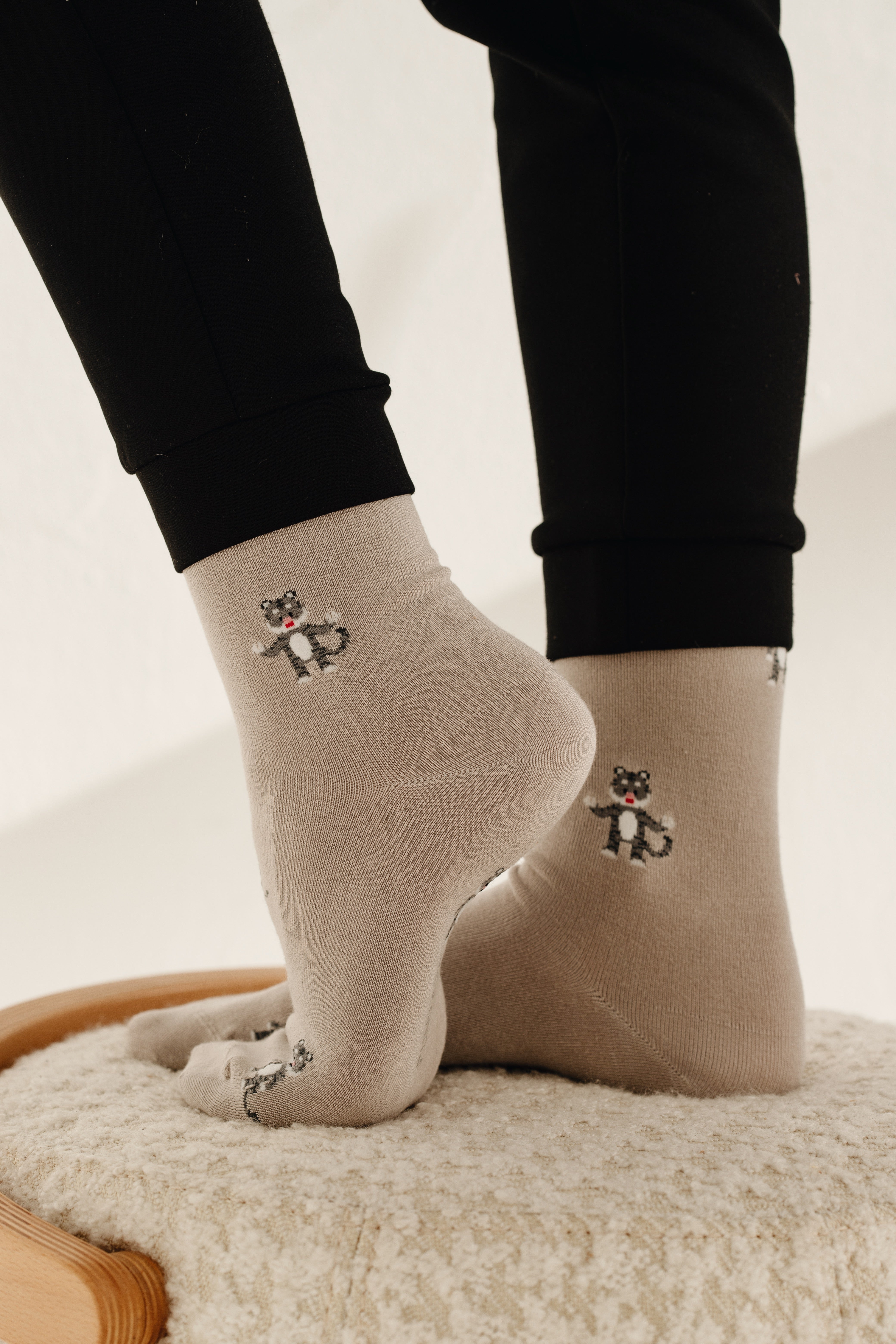 Rückansicht einer beige-melierten Socke am Fuß, die eine kleine Illustration eines stehenden Tieres mit gestreiftem Schwanz sowie den vertikalen Markenschriftzug „FUNDAZE“ zeigt.