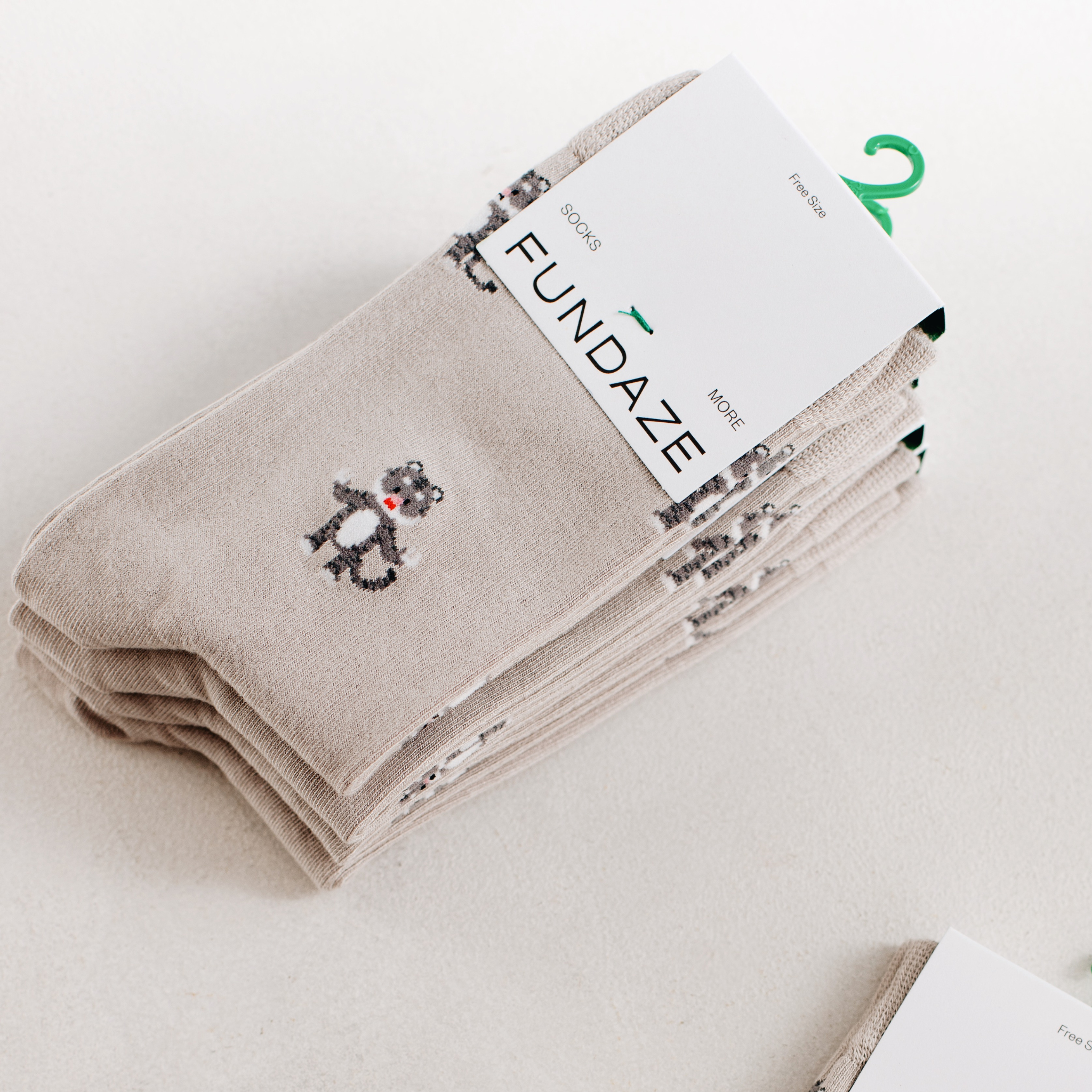 Ein ordentlich gestapeltes Set beige-melierter Socken mit Löwen-Print und weißer FUNDAZE-Markenbanderole auf hellem Untergrund.
