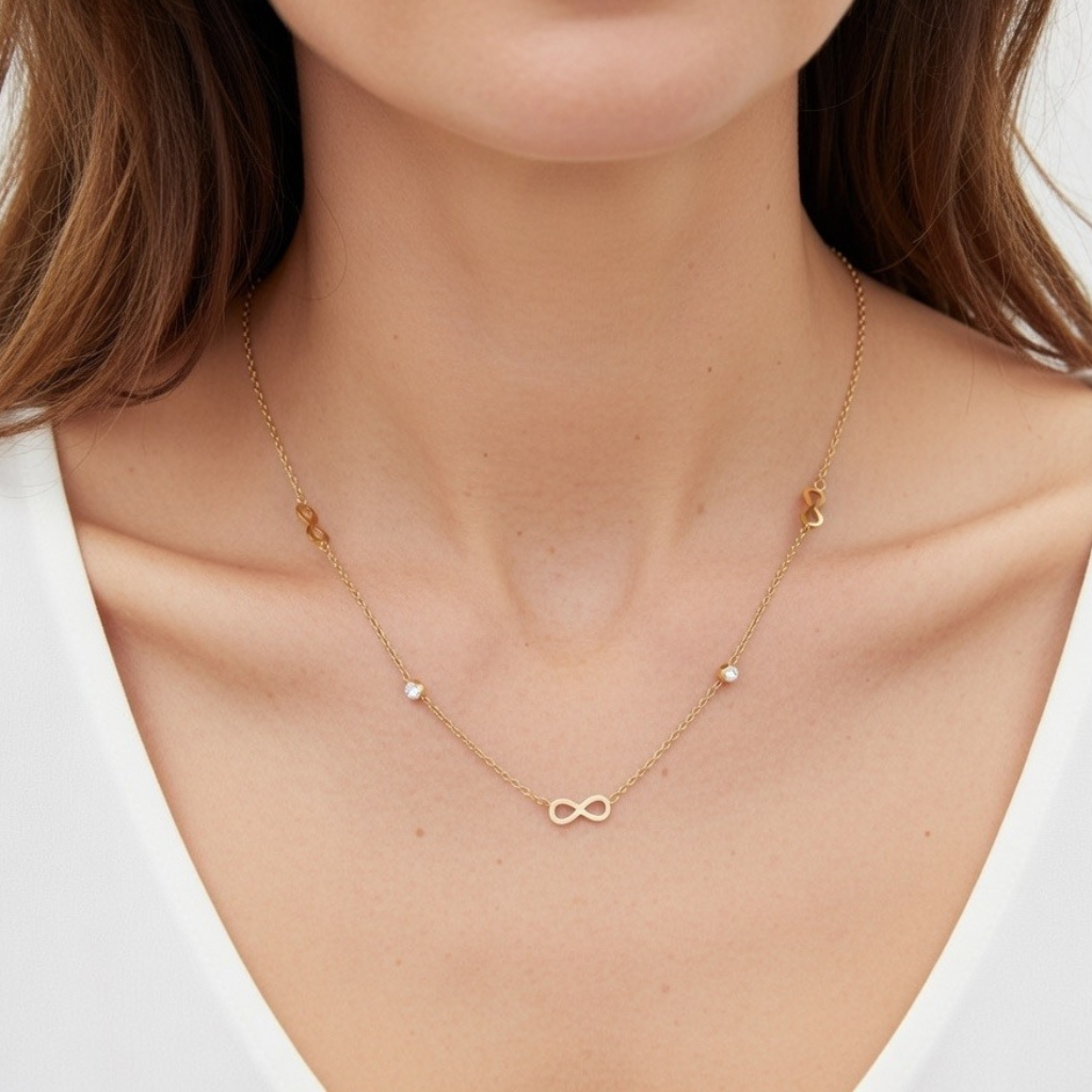 „Nahaufnahme einer Frau in einem weißen Oberteil, die eine feine goldene Halskette trägt. Das zentrale Element ist ein filigranes Unendlichkeitssymbol (Infinity), flankiert von zwei kleinen, funkelnden Zirkonia-Steinen und weiteren dezenten Infinity-Symbolen entlang der Kette.“