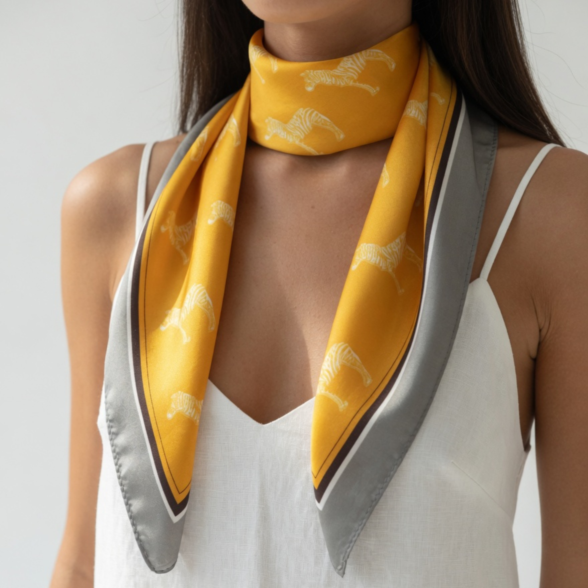 Ein leuchtend gelbes Halstuch mit Zebra-Motiven, das locker um den Hals eines Models liegt. Die grauen Enden hängen symmetrisch über ein helles Sommerkleid und betonen den eleganten, barrierefreien Modestil.