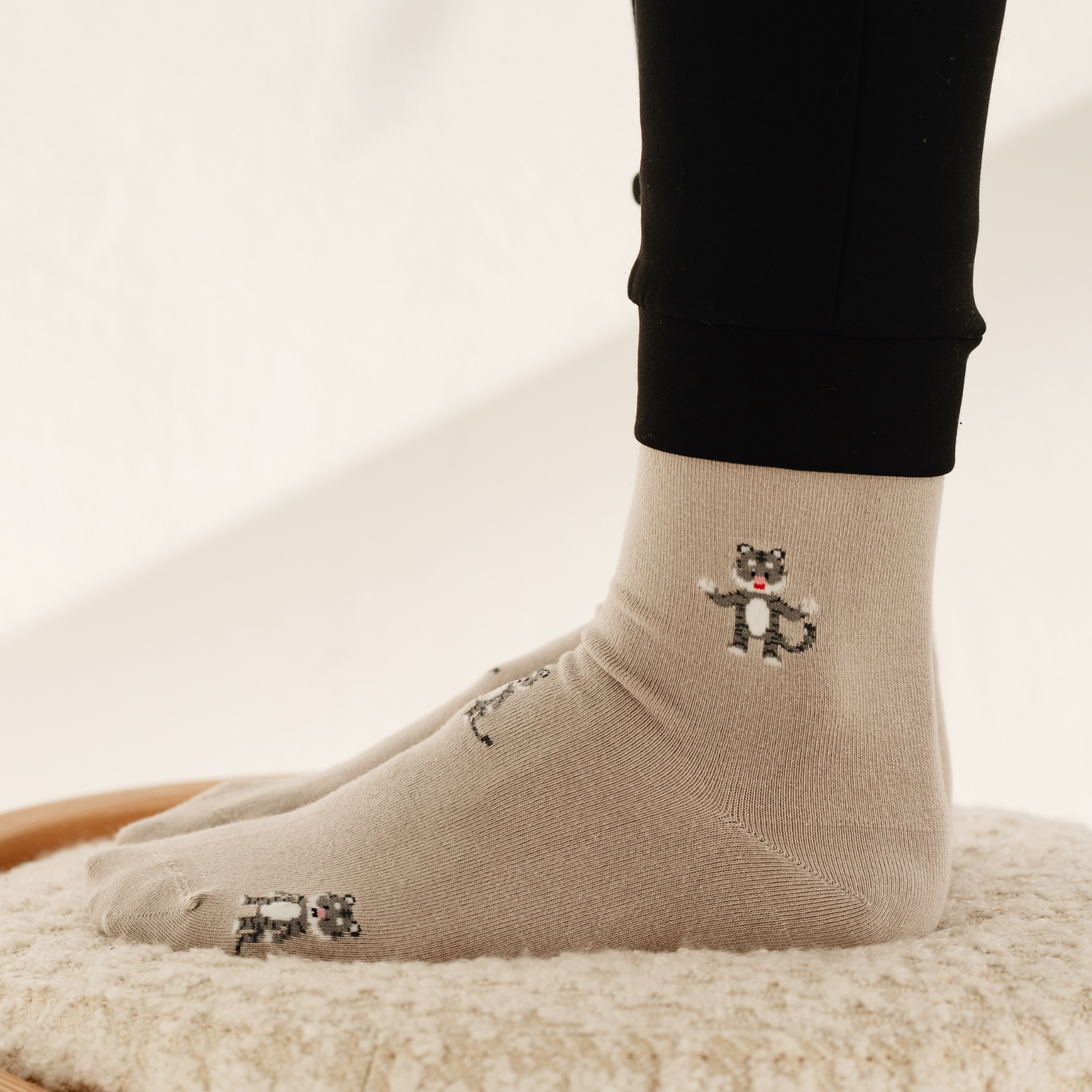 Nahaufnahme beider Füße in beigen FUNDAZE-Socken mit eingestickten Löwen-Motiven, die Beine sind in schwarzen Jogginghosen gekleidet.