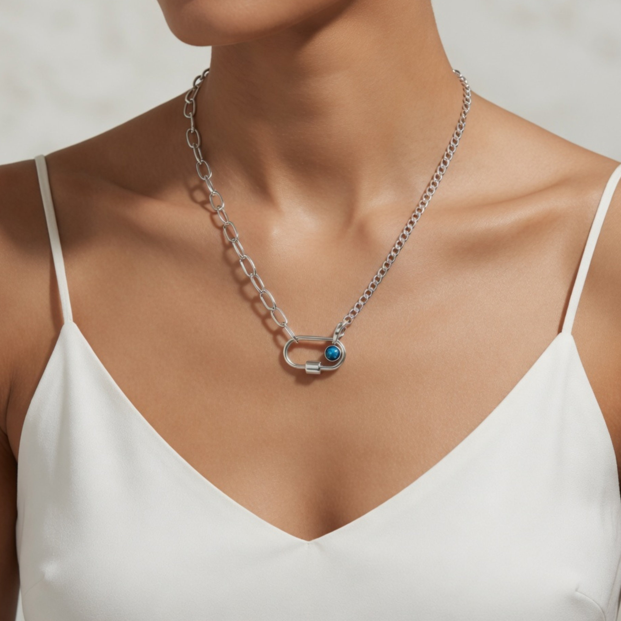 Nahaufnahme einer silbernen Halskette in asymmetrischem Design, bei der eine Seite aus klassischen Panzergliedern und die andere aus länglichen, ovalen Ösen besteht, fixiert durch einen silbernen Karabiner mit kleiner blauer Perle