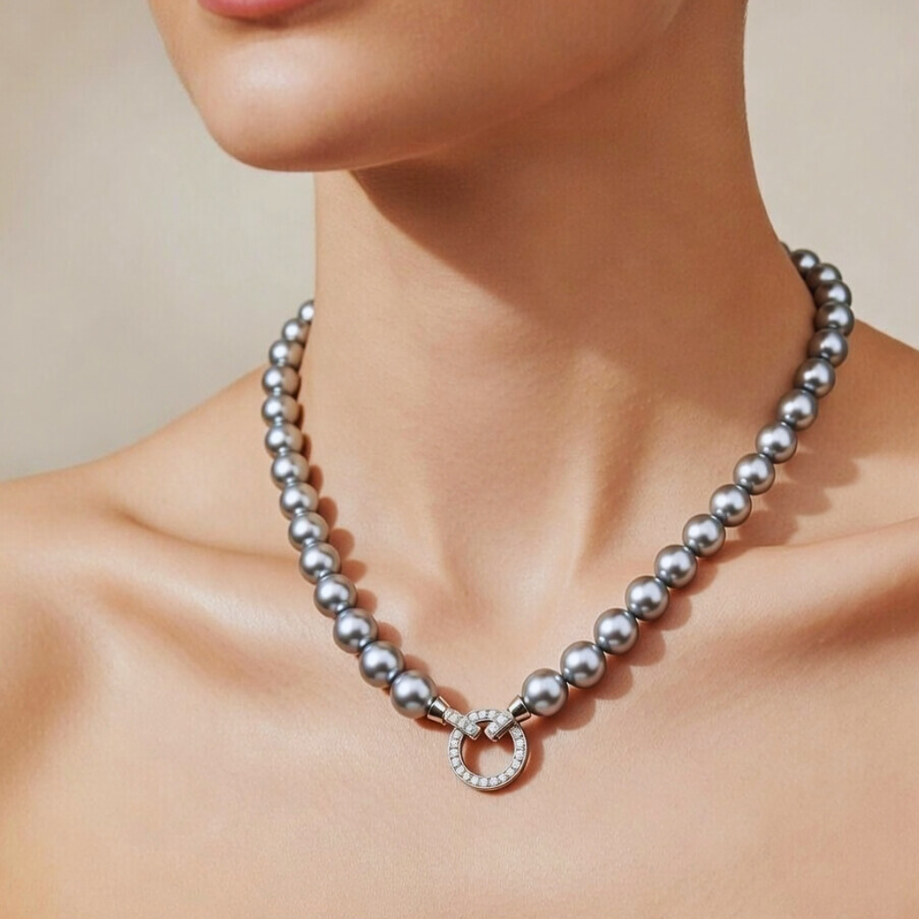 Nahaufnahme einer Frau, die eine einreihige Halskette aus großen, silbergrauen Perlen trägt. Die Kette wird vorne durch einen markanten, runden Ringverschluss geschlossen, der mit funkelnden Zirkonia-Steinen besetzt ist und als zentrales Schmuckelement dient